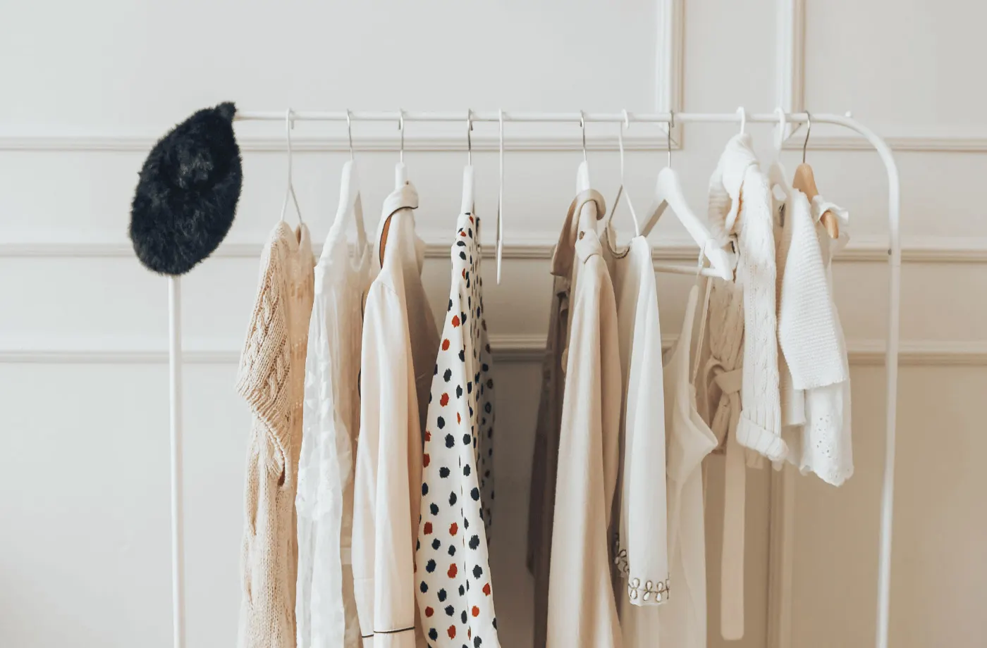 Cabideiro branco com roupas em tons claros e um chapéu de pelúcia preto